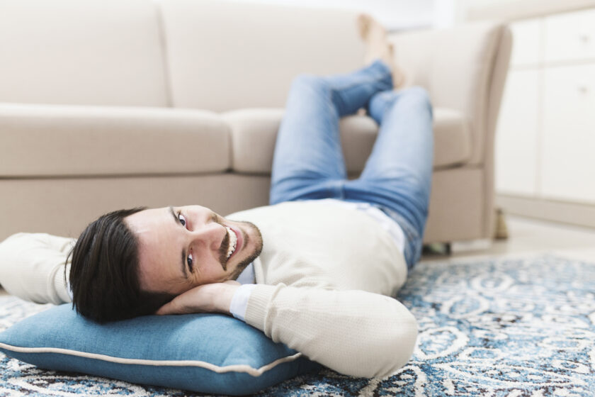 Attraktiver junger Mann liegt auf Teppich und entspannt nach der Arbeit