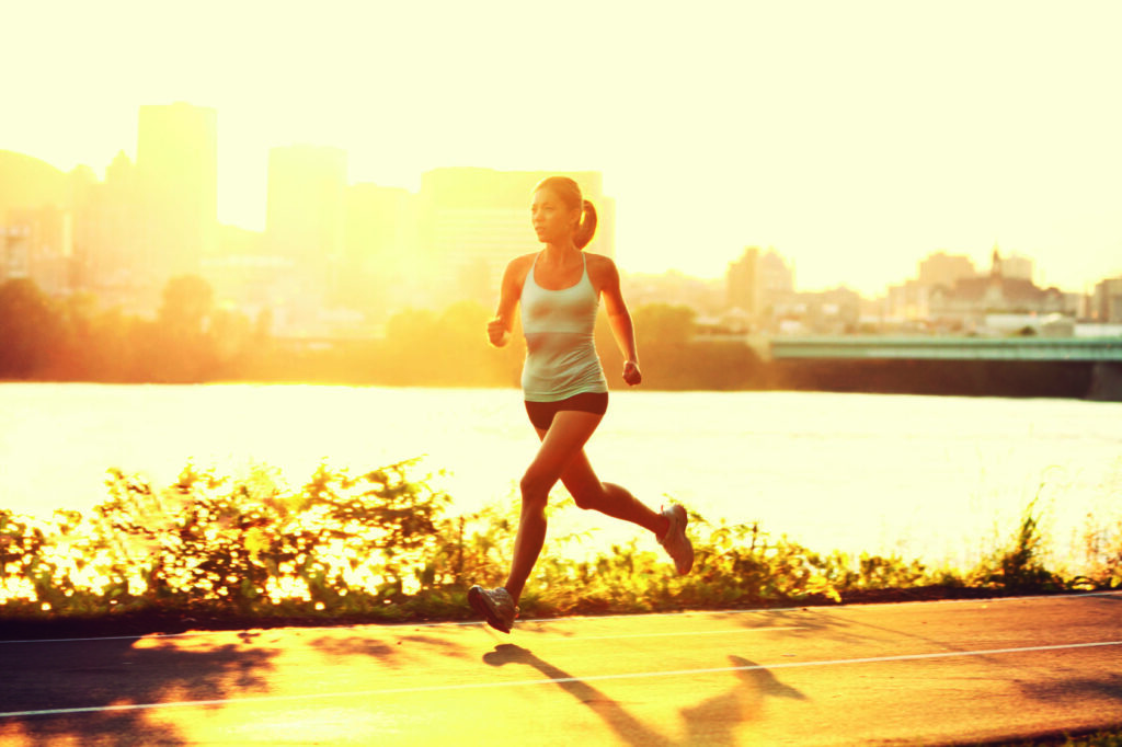 Frau beim Joggen während des Sonnenuntergangs am Fluss.