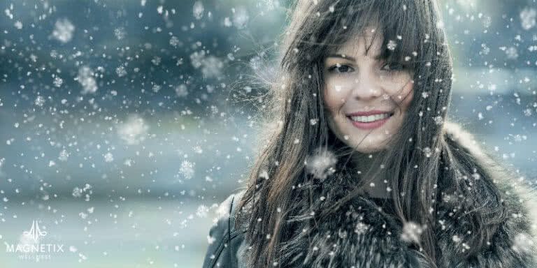 Im Bild ist eine lächelnde Frau mit langen braunen Haaren große Schneeflocken zu sehen.
